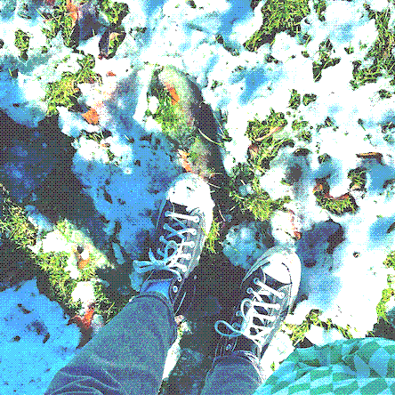 photo taken looking down the ground, showing the photographer's converse high top shoes standing in green grass with patches of melting snow. the grass is very bright green under the clumps of snow.