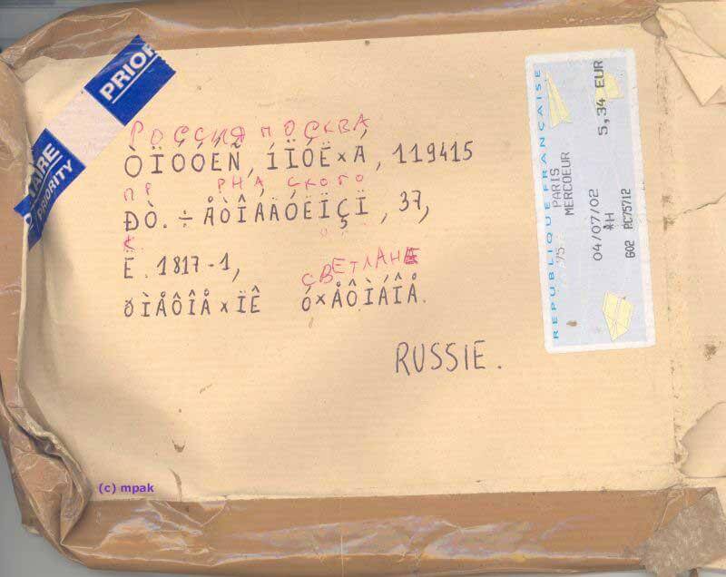 picture of a beat up package that was apparently sent to Russia back in 2002, judging by the date on the label. the address on the package is unintelligble because it's handwritten gibberish. someone has written the correct Cyrillic characters above the gibberish address.